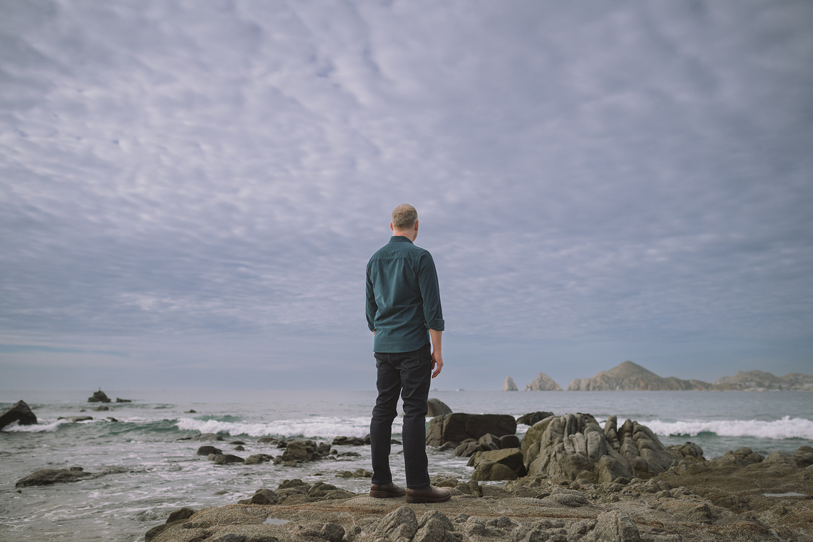Jeffrey Van Dyk standing on a rocky coastline, looking out at the sea