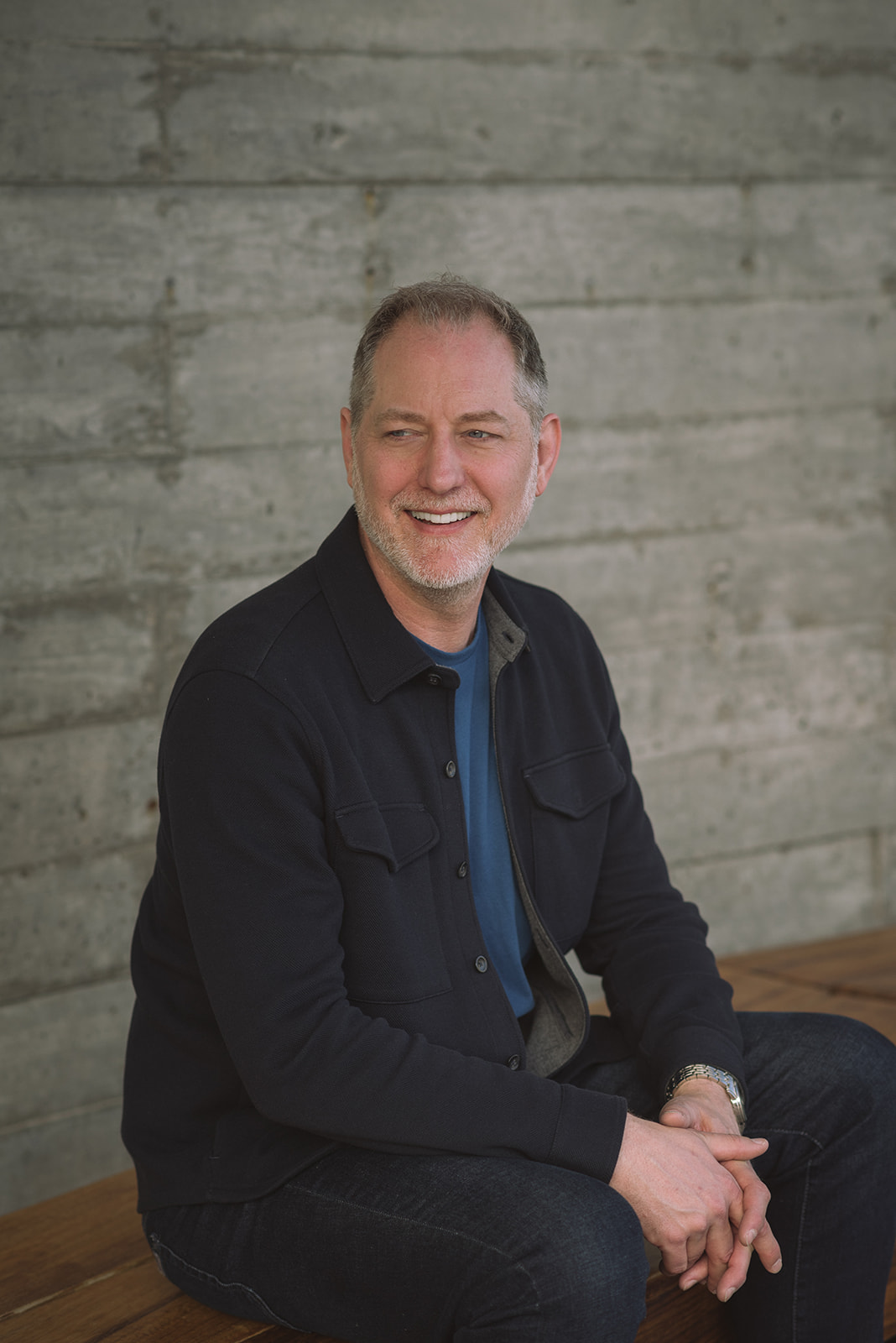 Jeffrey Van Dyk smiling, seated against a concrete wall