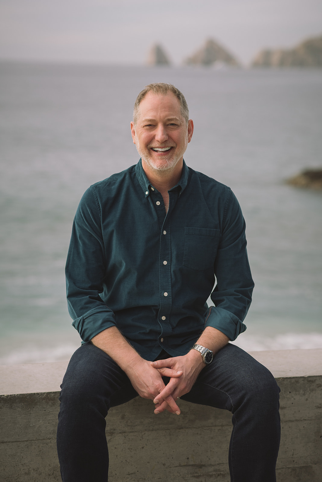 Jeffrey Van Dyk smiling, seated with the ocean behind him
