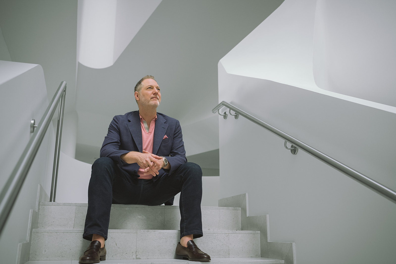 Jeffrey Van Dyk seated, looking upward in a modern stairwell